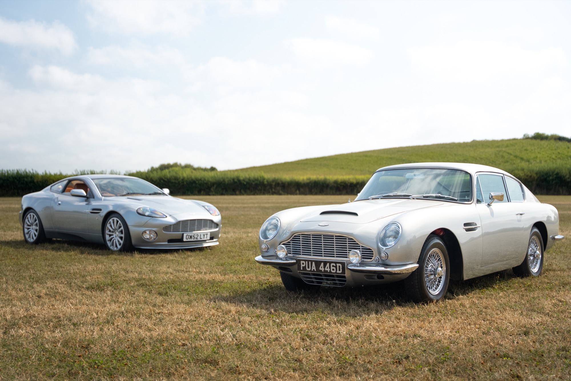 Silver Aston Martin DB6 and Vanquish in a field