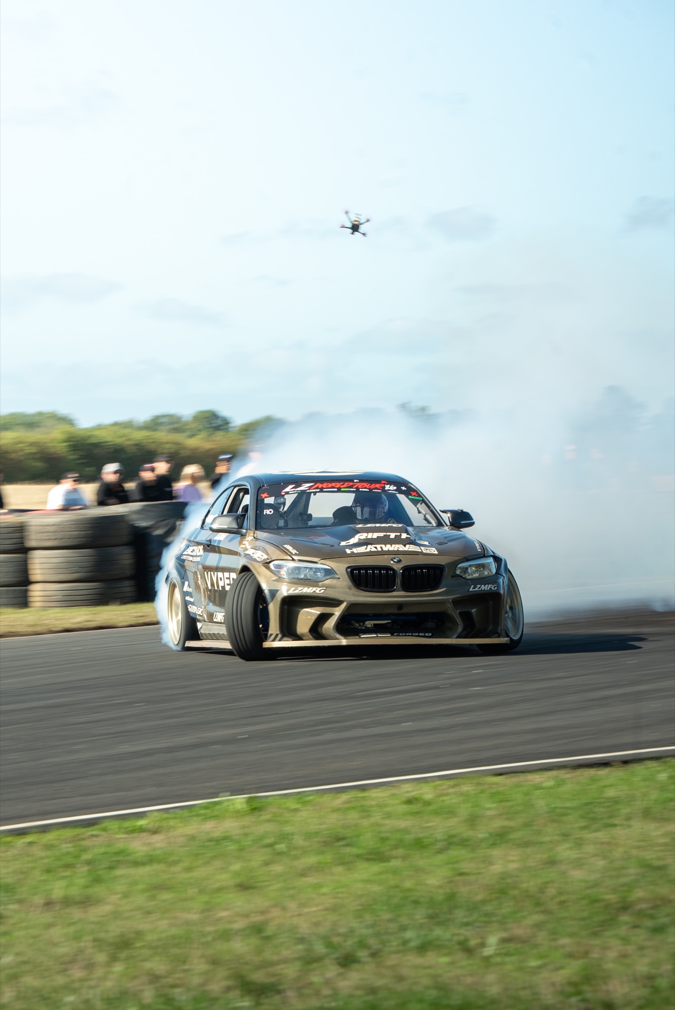 Bronze BMW M2 drifting at LZ World Tour, smoke in the air and a drone overhead