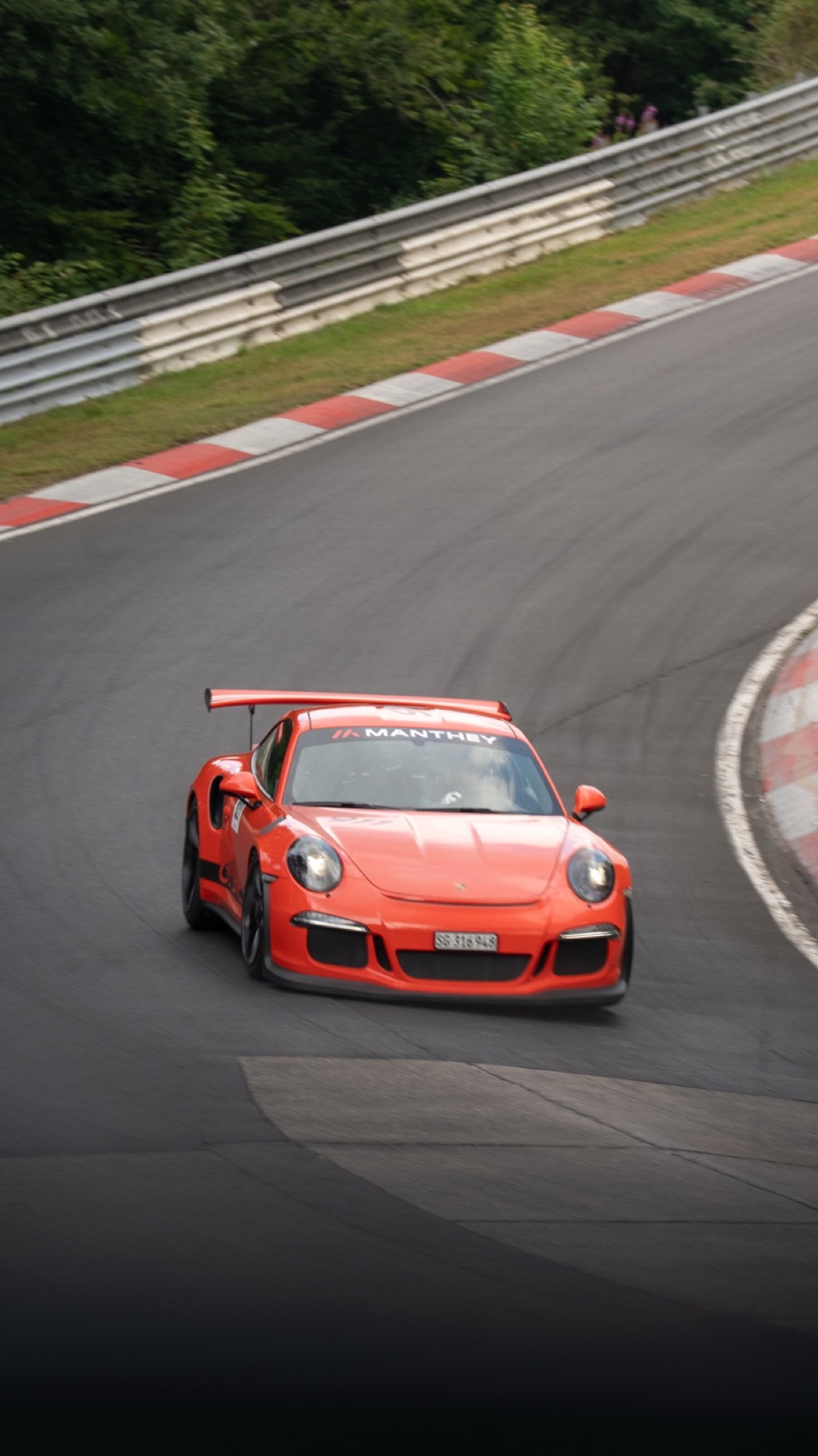 Orange Porsche 911 GT3 Manthey climbing a Nürburgring corner
